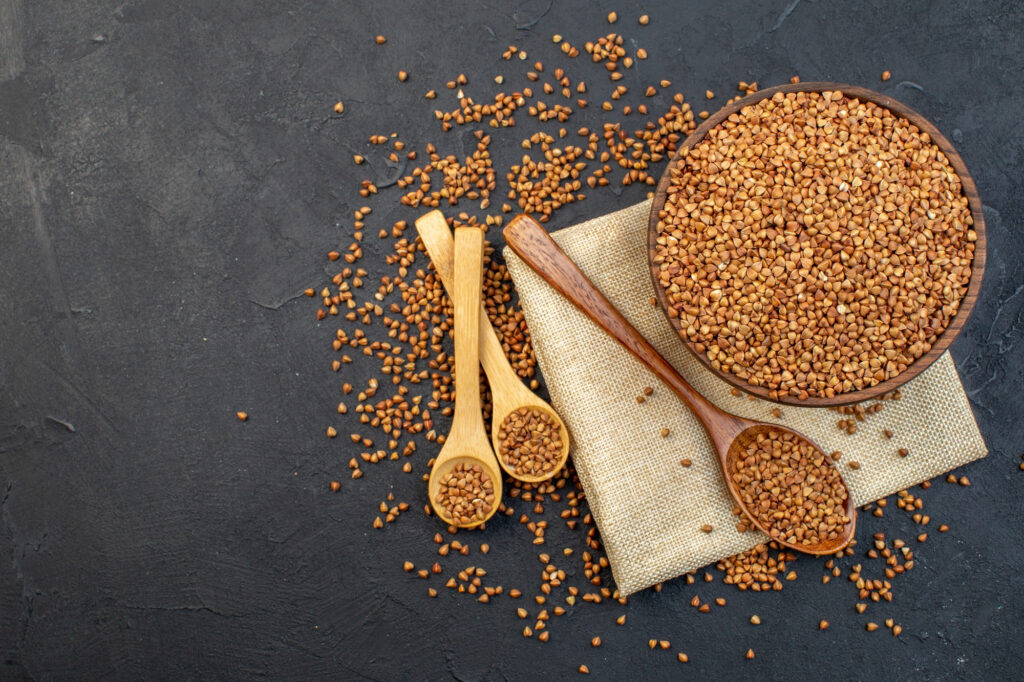 top view brown buckwheat inside plate with pair spoons dark background